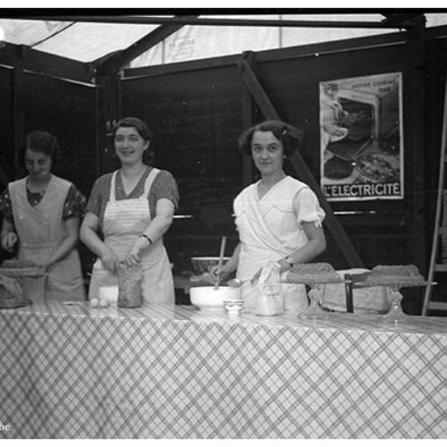 Démonstration de cuisinières électriques à la demande de la S.A. Electricité de la Dendre, à l'emplacement de l'ancienne pharmacie Vanderelst. De droite à gauche Hermans Duquenne, une Lessinoise et Gabrielle Duquenne.